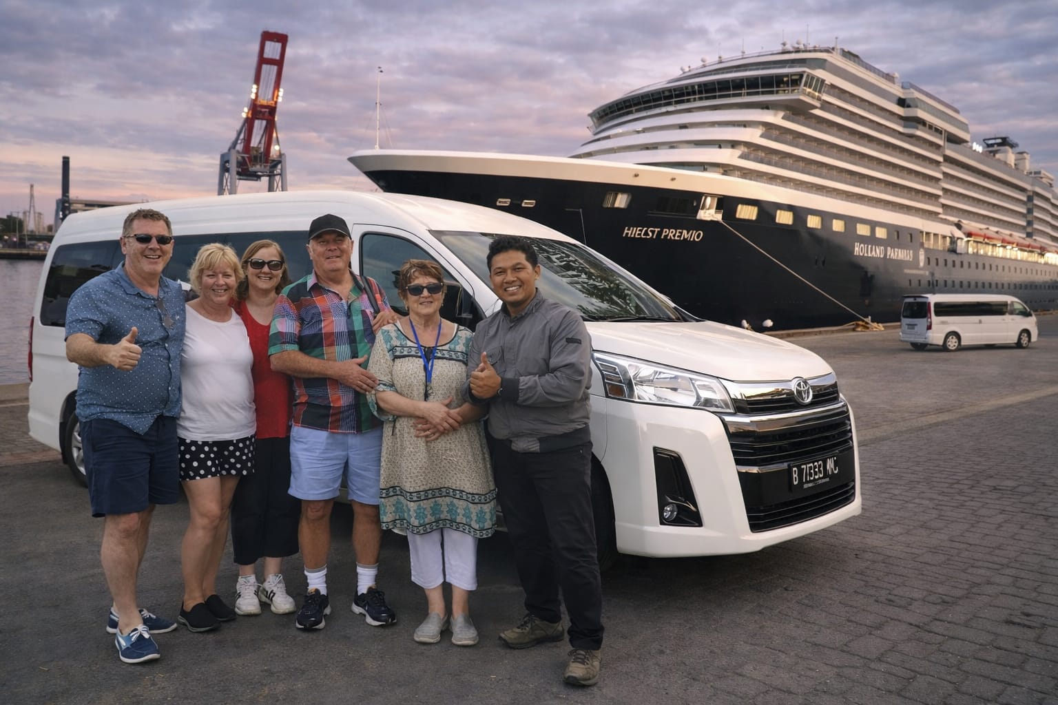 Group of tourists with a local guide standing in front of a Toyota HiAce Premio van at a cruise ship port in Indonesia during sunset